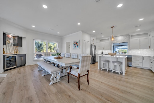 dining room featuring wine cooler, crown molding, sink, and light wood-type flooring