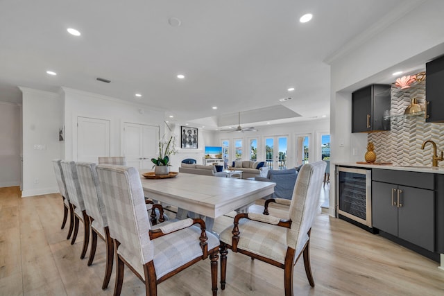 dining area featuring beverage cooler, ceiling fan, sink, crown molding, and light hardwood / wood-style flooring