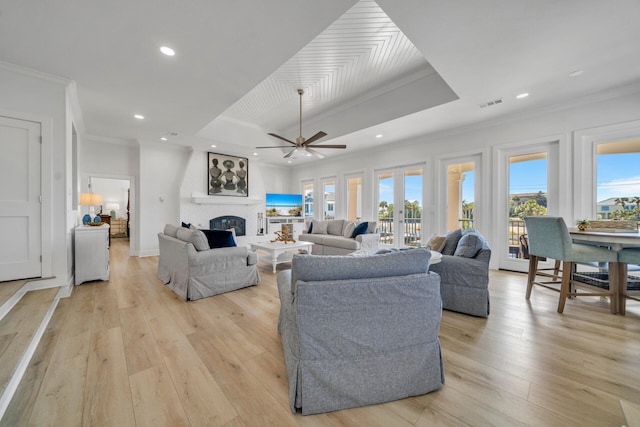 living room featuring a raised ceiling, light hardwood / wood-style floors, ceiling fan, and a fireplace