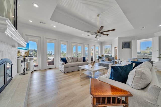 living room featuring a tray ceiling, ceiling fan, light hardwood / wood-style floors, and a brick fireplace