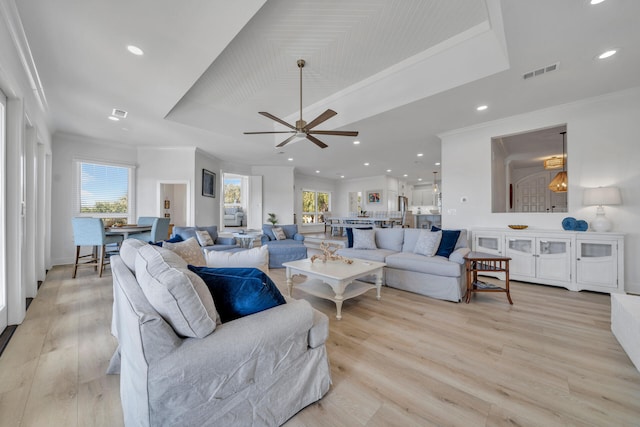 living room with light hardwood / wood-style flooring, ceiling fan, and a tray ceiling