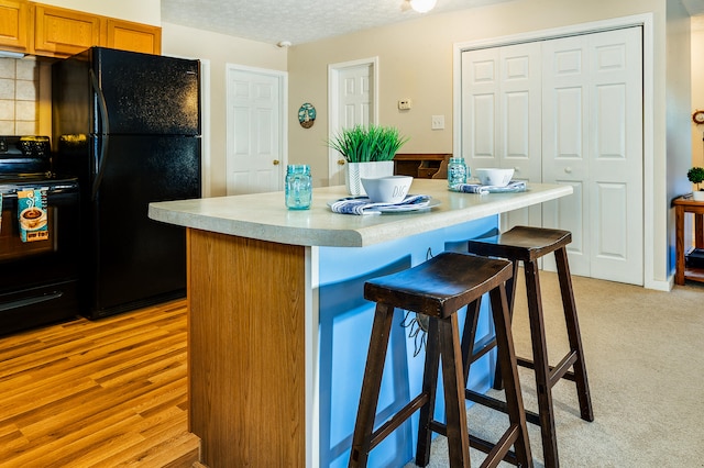 kitchen with a breakfast bar, a kitchen island, a textured ceiling, black appliances, and light hardwood / wood-style flooring