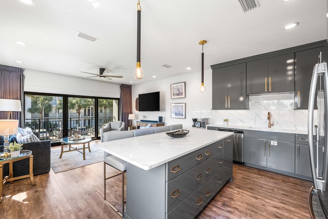 kitchen with a center island, decorative light fixtures, gray cabinetry, light stone counters, and ceiling fan