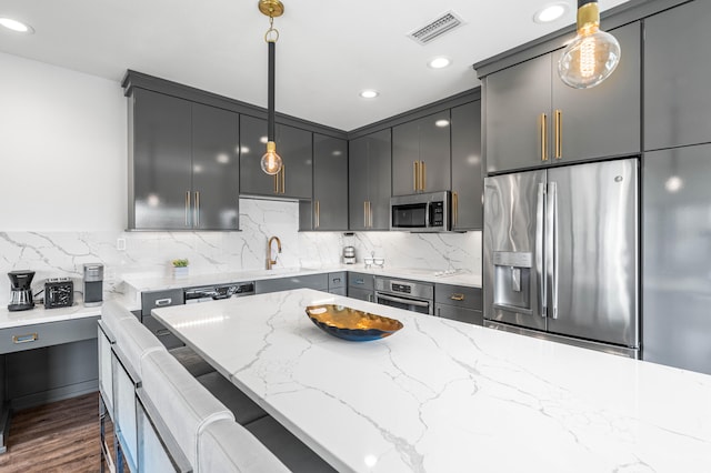 kitchen with gray cabinets, pendant lighting, appliances with stainless steel finishes, and light stone counters