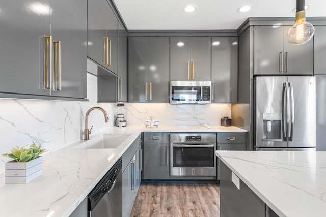 kitchen with appliances with stainless steel finishes, gray cabinetry, backsplash, and light stone counters