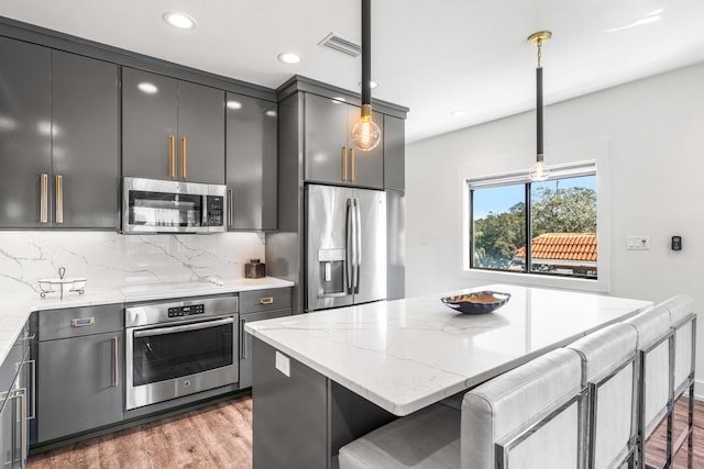 kitchen with appliances with stainless steel finishes, light stone counters, a breakfast bar area, and decorative light fixtures