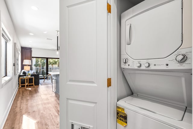 laundry room with light wood-type flooring and stacked washer / drying machine