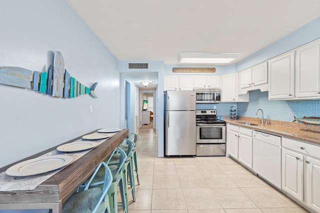 kitchen featuring visible vents, light stone countertops, stainless steel appliances, white cabinetry, and a sink