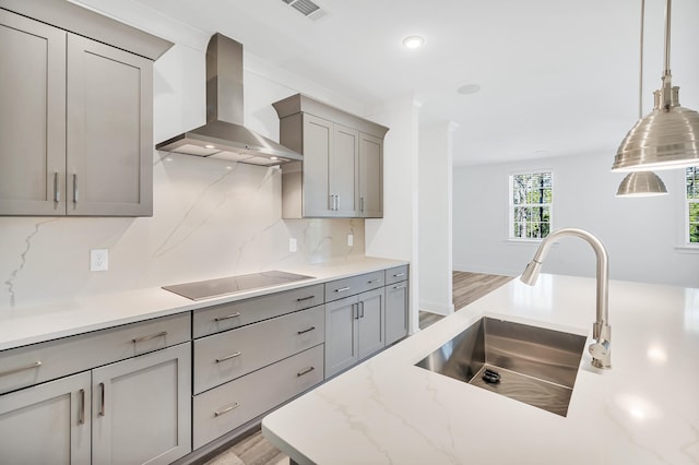 kitchen with wall chimney range hood, light hardwood / wood-style floors, black electric cooktop, and backsplash