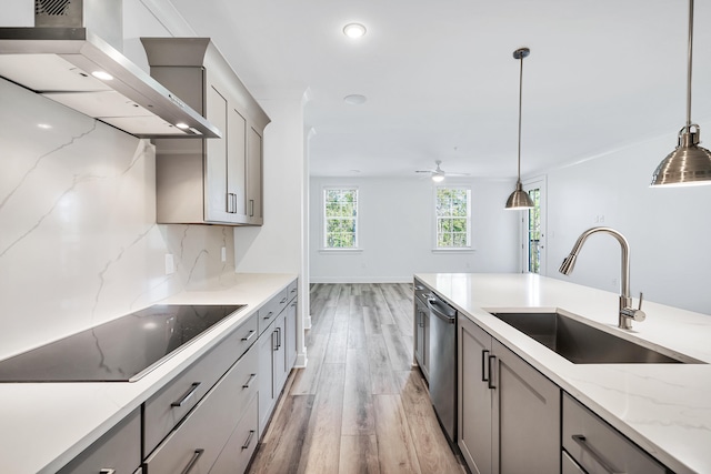 kitchen featuring light hardwood / wood-style floors, black electric cooktop, pendant lighting, wall chimney exhaust hood, and sink