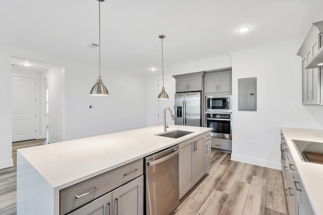 kitchen with stainless steel appliances, a center island with sink, decorative light fixtures, light wood-type flooring, and sink