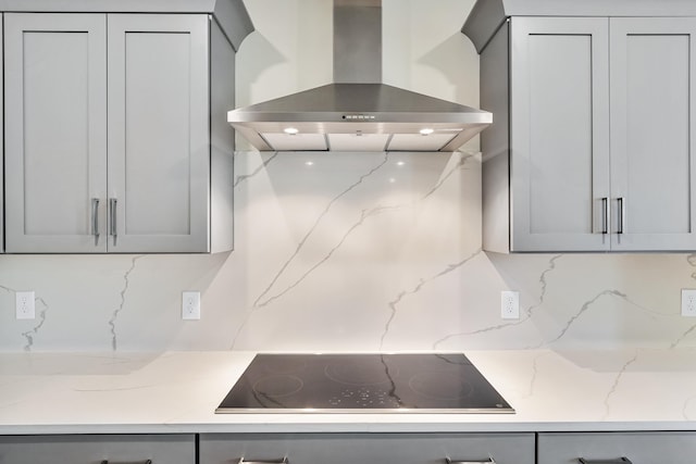 kitchen featuring wall chimney exhaust hood, gray cabinets, black electric cooktop, and backsplash