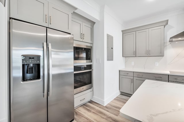 kitchen with crown molding, light stone countertops, light wood-type flooring, gray cabinetry, and stainless steel appliances