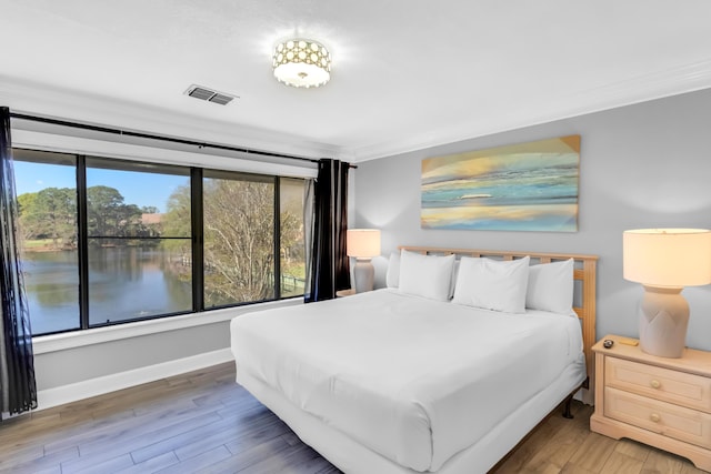 bedroom featuring hardwood / wood-style floors, a water view, and ornamental molding