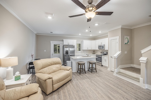 living room featuring ceiling fan, light wood-type flooring, sink, and ornamental molding