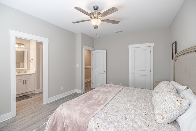 bedroom featuring a closet, light hardwood / wood-style flooring, ensuite bathroom, ceiling fan, and sink