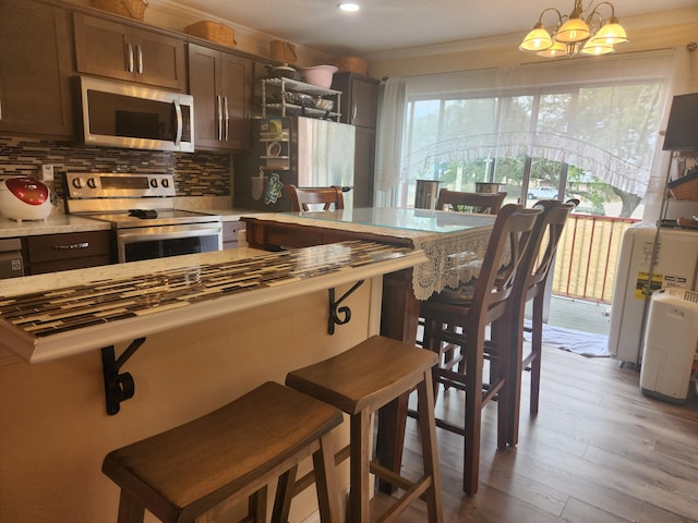 kitchen with hanging light fixtures, light hardwood / wood-style flooring, stainless steel appliances, tasteful backsplash, and a chandelier