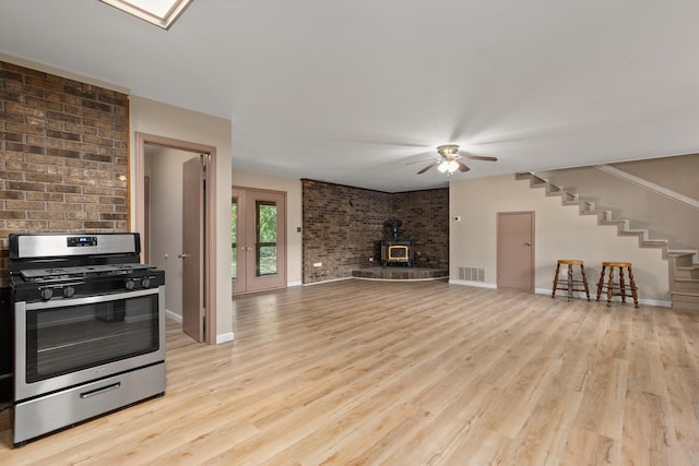 kitchen with light hardwood / wood-style floors, stainless steel range with gas stovetop, ceiling fan, and a wood stove