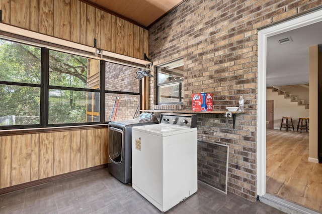 laundry room featuring brick wall, wooden walls, and washer and clothes dryer