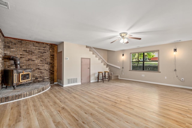 unfurnished living room featuring light wood-type flooring, ceiling fan, and a wood stove