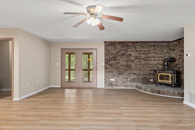 unfurnished living room with french doors, light hardwood / wood-style flooring, a wood stove, ceiling fan, and brick wall