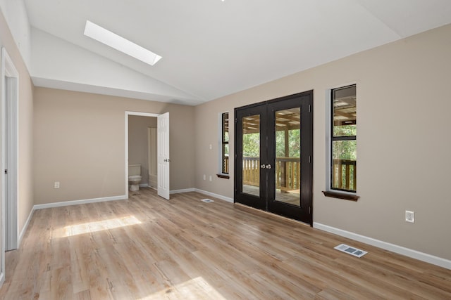 unfurnished room featuring lofted ceiling with skylight, light wood-type flooring, and french doors