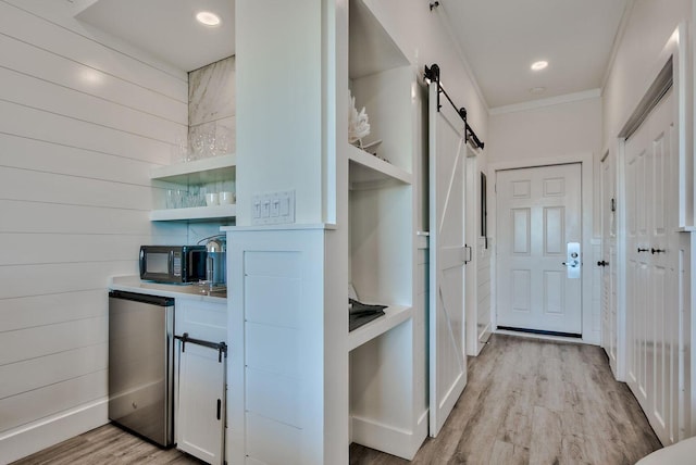 kitchen featuring white cabinets, refrigerator, crown molding, a barn door, and light hardwood / wood-style floors