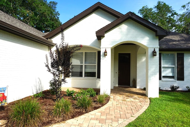 entrance to property featuring a yard, brick siding, and roof with shingles