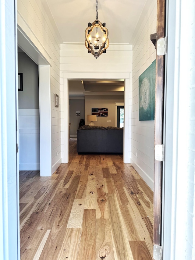 hallway featuring an inviting chandelier, wooden walls, baseboards, and wood finished floors