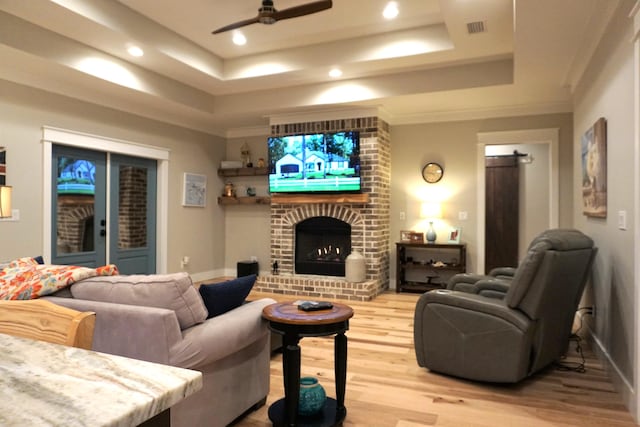 living room featuring a fireplace, wood finished floors, visible vents, a ceiling fan, and a raised ceiling