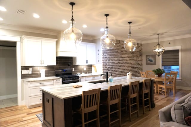 kitchen with white cabinets, range, decorative light fixtures, a kitchen island with sink, and a sink