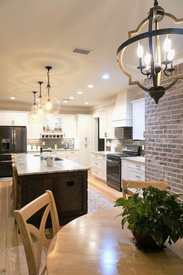 kitchen with range with gas stovetop, glass insert cabinets, hanging light fixtures, light countertops, and white cabinetry