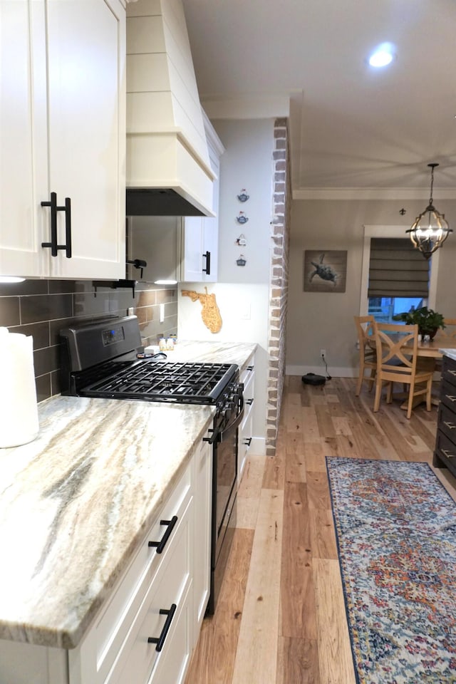 kitchen with custom exhaust hood, black range with gas cooktop, white cabinetry, and light stone counters