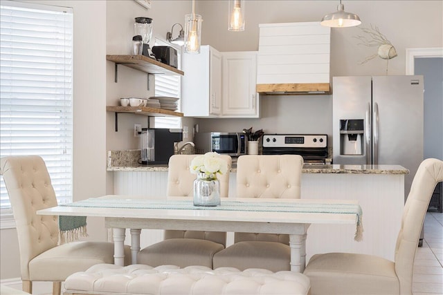 kitchen with hanging light fixtures, white cabinets, appliances with stainless steel finishes, a kitchen bar, and light stone counters