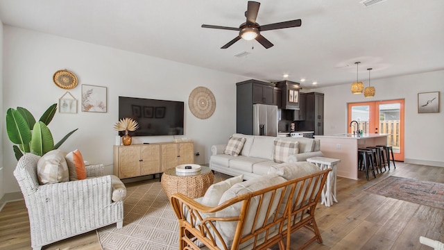 living room featuring light hardwood / wood-style flooring, french doors, ceiling fan, and sink