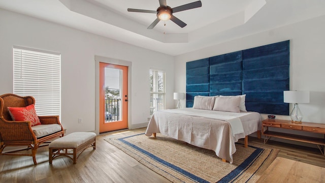 bedroom featuring ceiling fan, access to exterior, a tray ceiling, and dark wood-type flooring