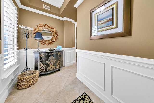 hallway featuring light tile patterned floors, visible vents, a wainscoted wall, ornamental molding, and a decorative wall