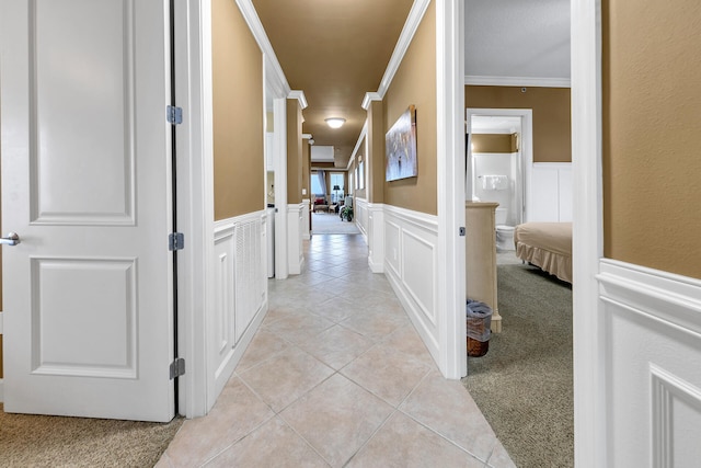 hall with light carpet, wainscoting, crown molding, a decorative wall, and light tile patterned flooring