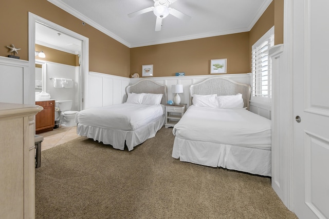 bedroom featuring a wainscoted wall, light carpet, ensuite bath, and crown molding