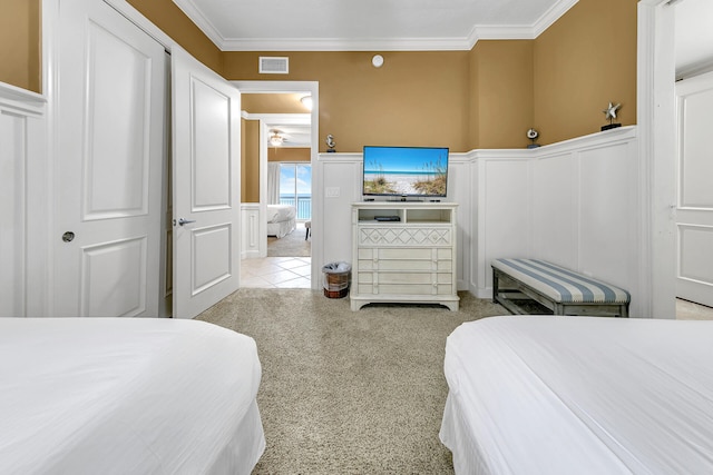 bedroom with a wainscoted wall, crown molding, light colored carpet, visible vents, and a decorative wall