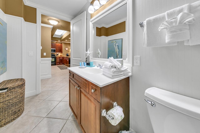 bathroom featuring toilet, a decorative wall, ornamental molding, tile patterned floors, and a raised ceiling