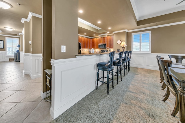 kitchen featuring light tile patterned floors, a decorative wall, a peninsula, a breakfast bar, and stainless steel microwave