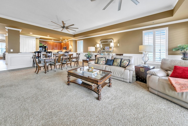 living room featuring a wainscoted wall, a decorative wall, a ceiling fan, ornamental molding, and light carpet