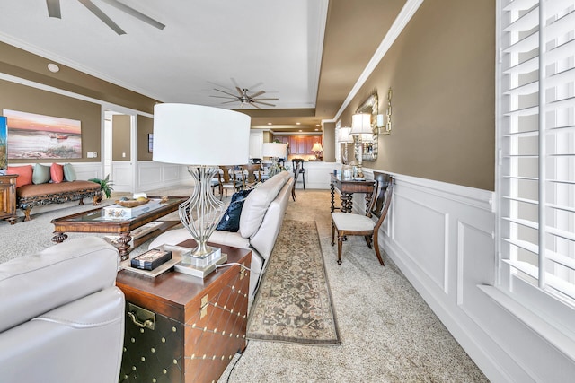 carpeted living room featuring a decorative wall, wainscoting, a ceiling fan, and crown molding