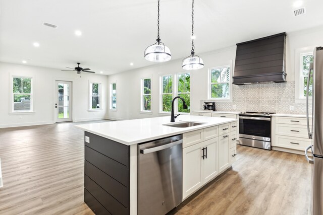 kitchen featuring white cabinets, custom exhaust hood, stainless steel appliances, sink, and a center island with sink