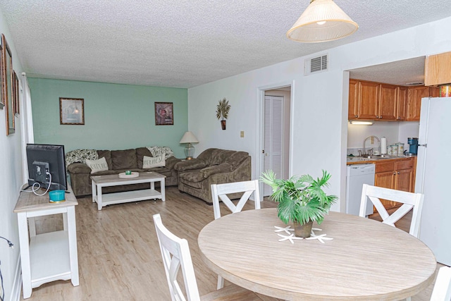 dining area with light hardwood / wood-style flooring, sink, and a textured ceiling