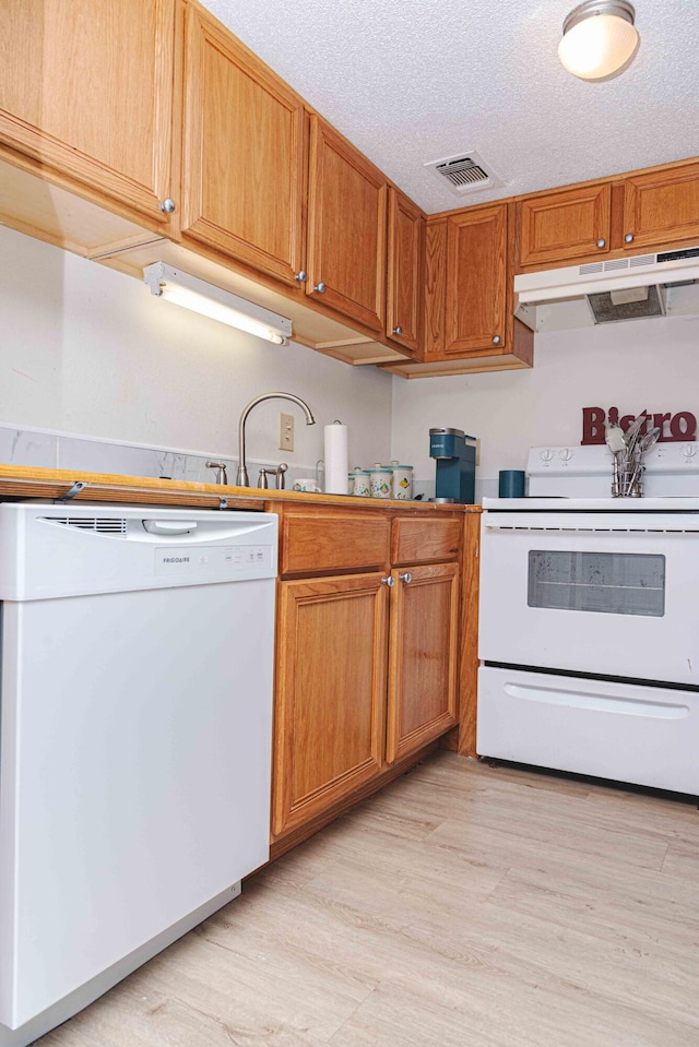 kitchen with a textured ceiling, white appliances, and light wood-type flooring