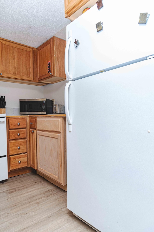 kitchen with white fridge, light hardwood / wood-style flooring, a textured ceiling, and range