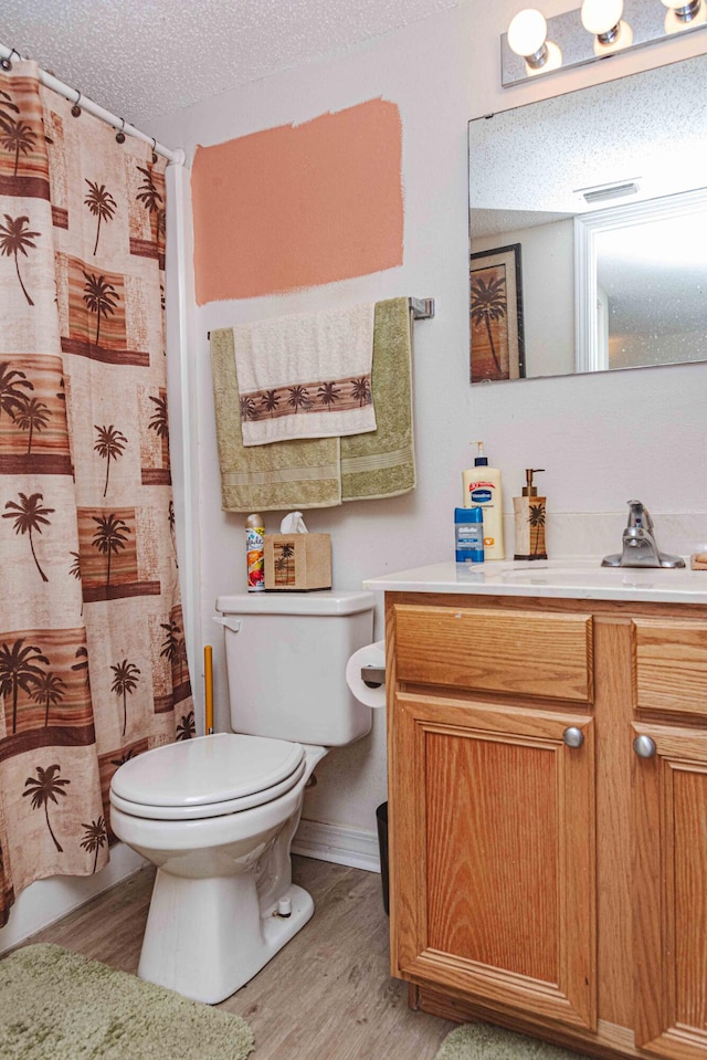 bathroom with wood-type flooring, toilet, vanity, and a textured ceiling