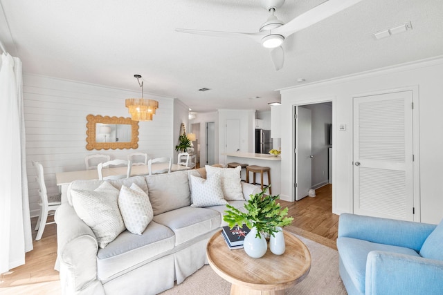 living room with ceiling fan with notable chandelier, ornamental molding, and light hardwood / wood-style floors